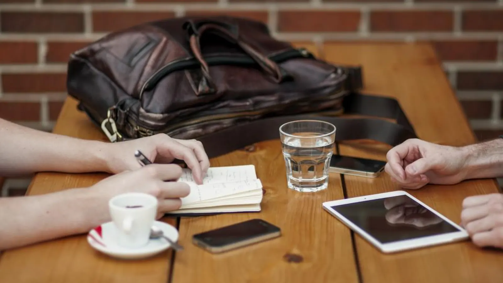 Two people meeting at a cafe table with a tablet and notebook