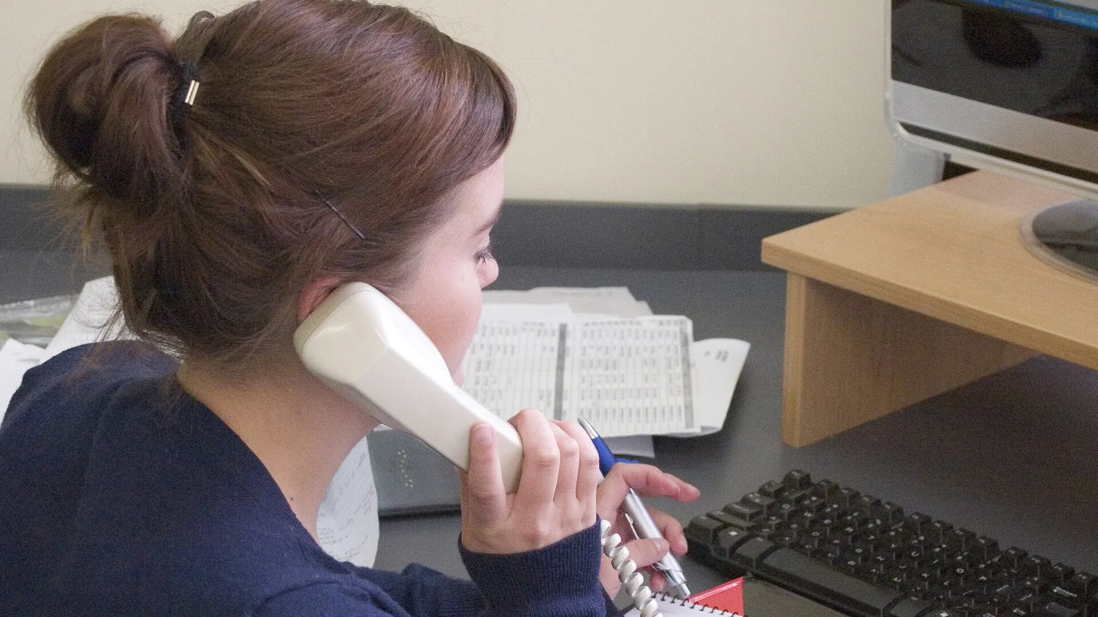 Office worker holding a desk phone while typing